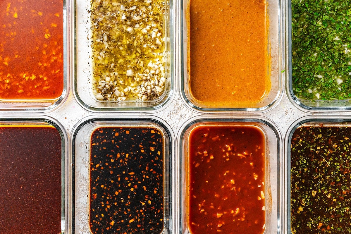 Eight clear containers filled with different sauces, dressings, and tofu marinades—each with varying colors and visible herbs, spices, or oil—are arranged in a neat grid.