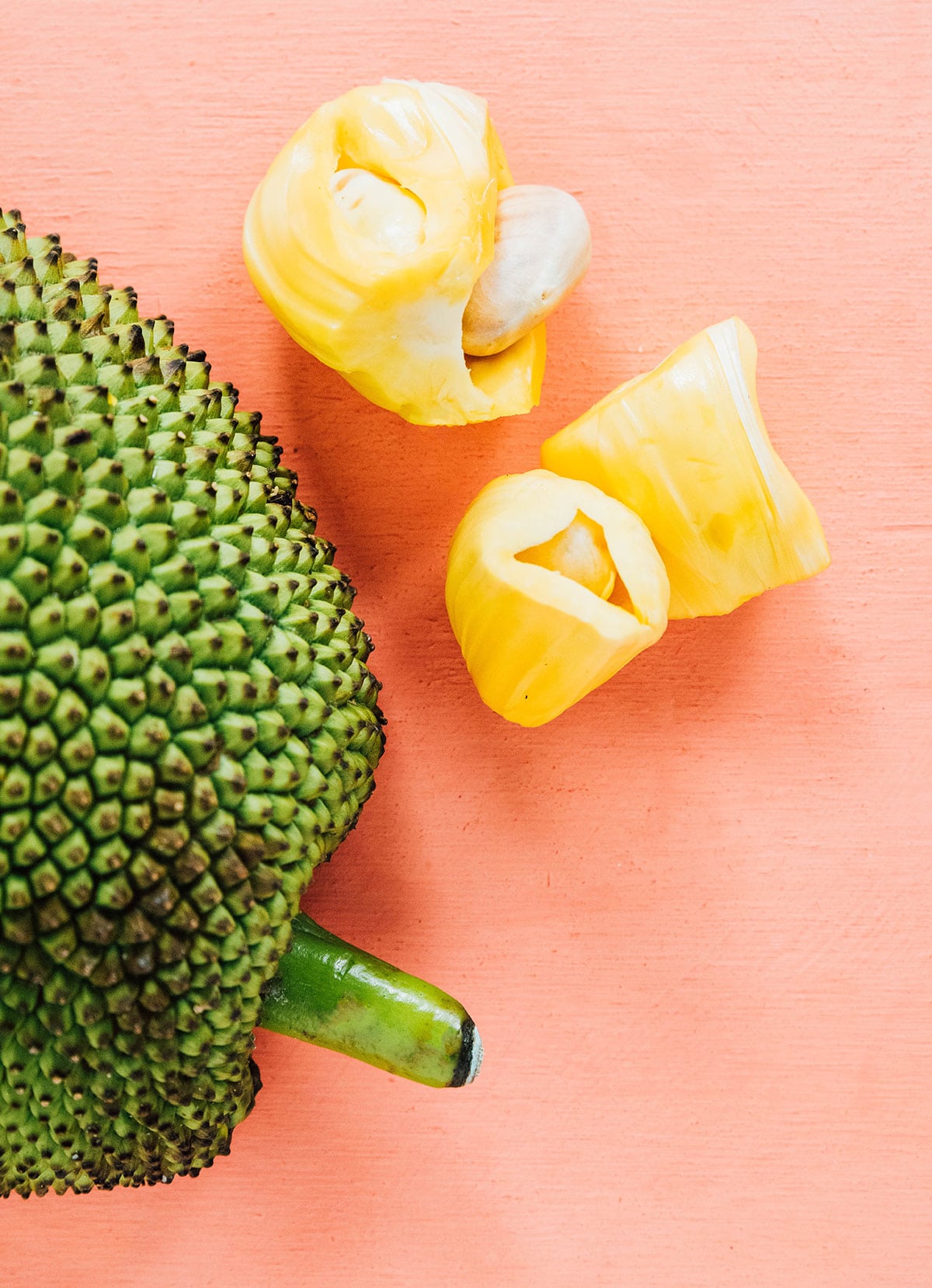 Jackfruit seeds in their yellow pods next to the skin of the jackfruit.