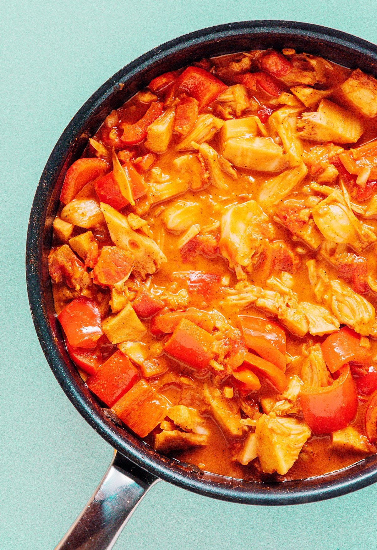 Jackfruit curry in a pan after cooking that is bright orange in color.