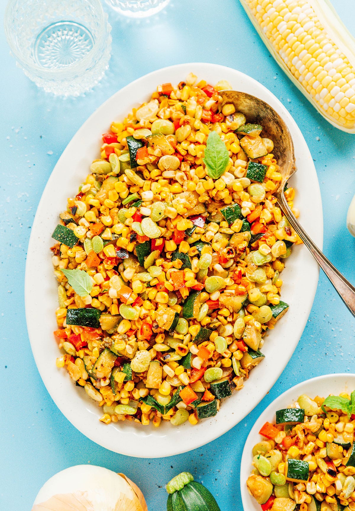 Succotash on a plate with a spoon and corn beside it.