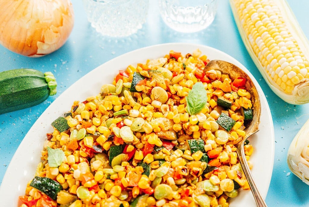 Succotash on a plate with a spoon scooping some out.
