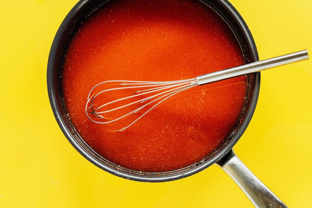 A whisk in a pot of tomato sauce.