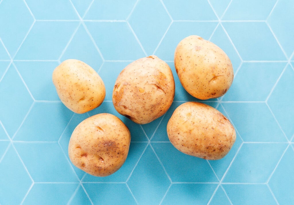 5 washed potatoes on a blue surface.