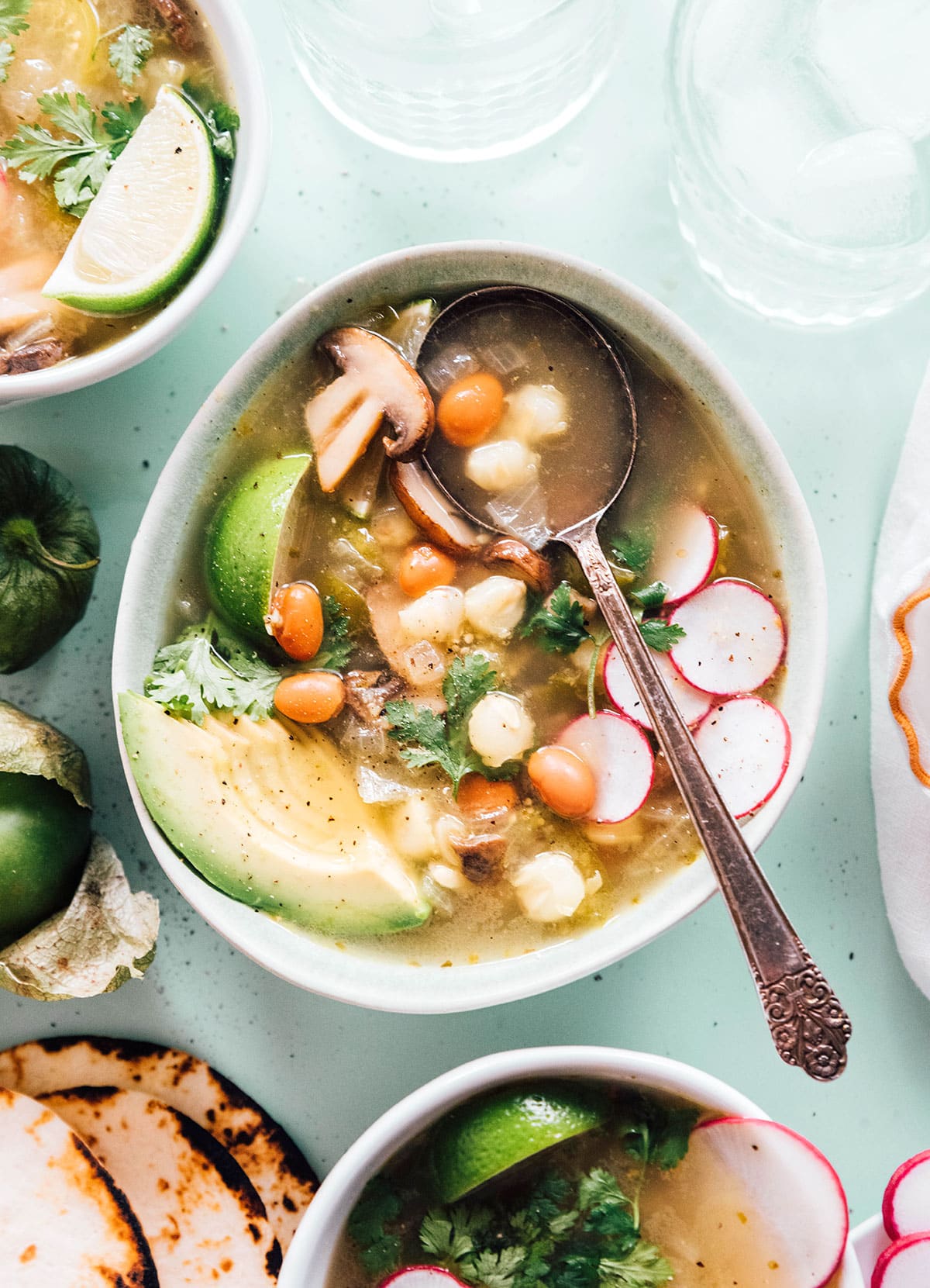 Pozole verde with sliced radishes and avocado in a bowl with a spoon
