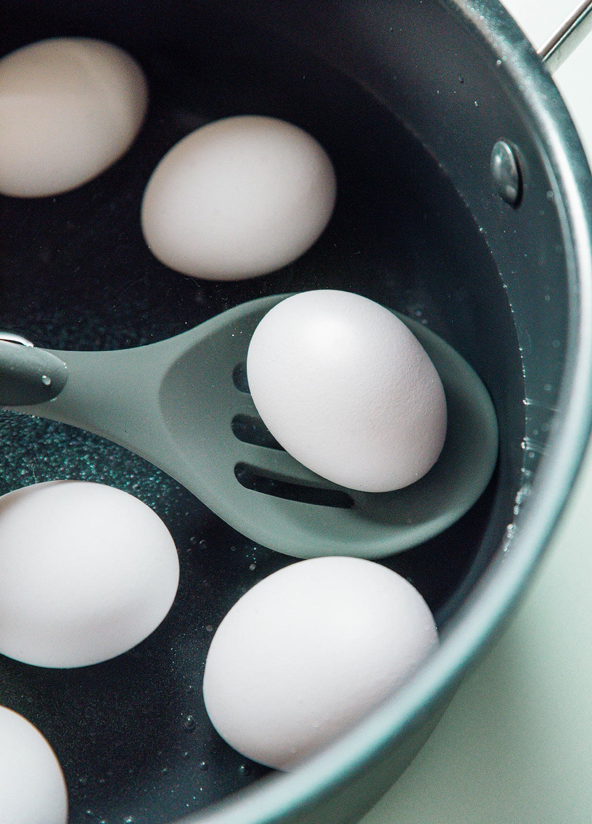 A slotted spoon removing boiled eggs from a pot of water.