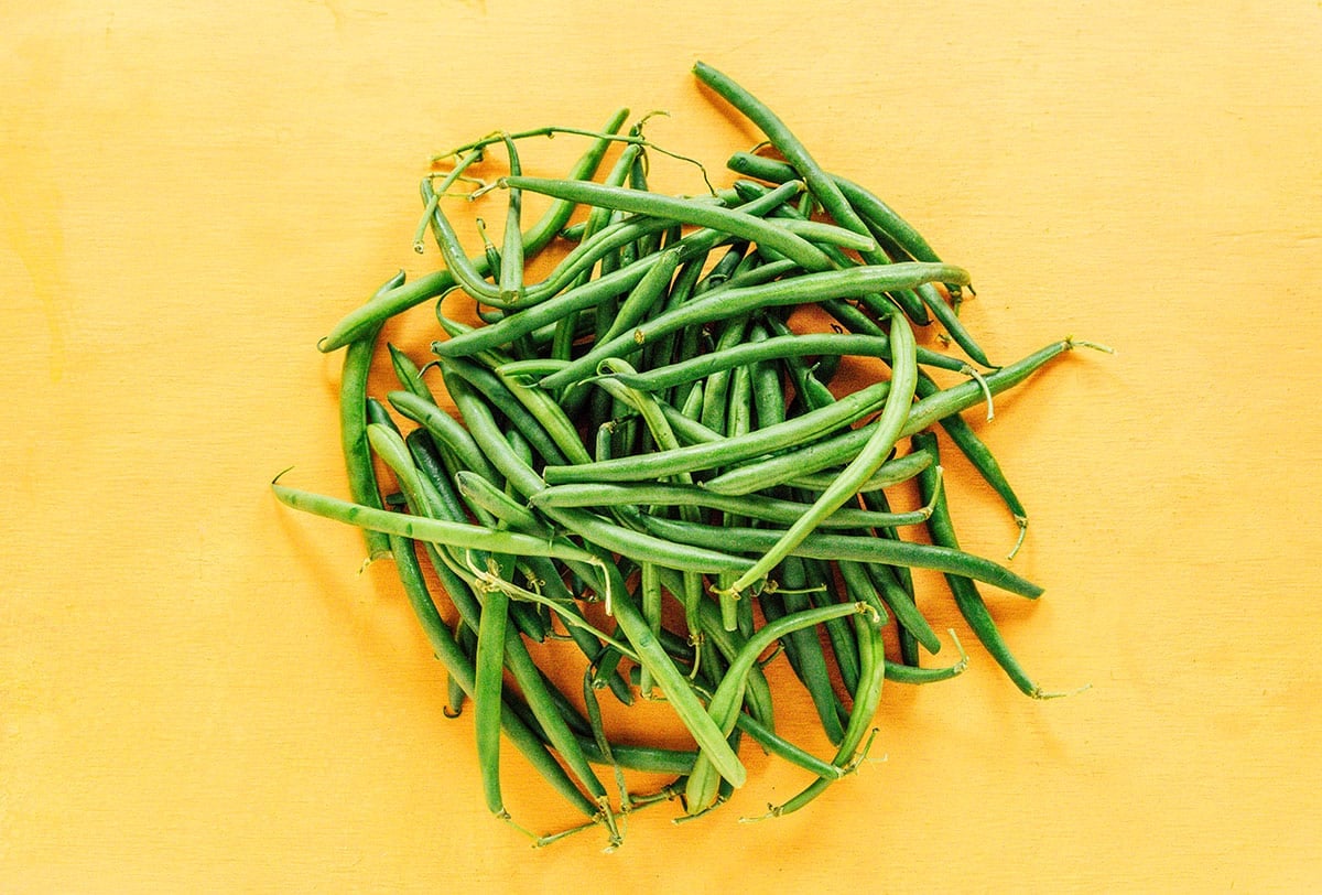 Raw geren beans in a pile on an orange surface.