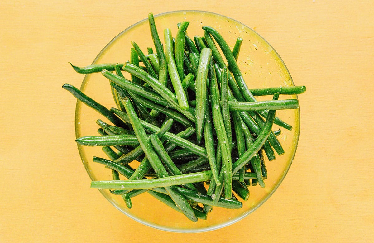 Oiled and seasoned green beans in a glass mixing bowl.