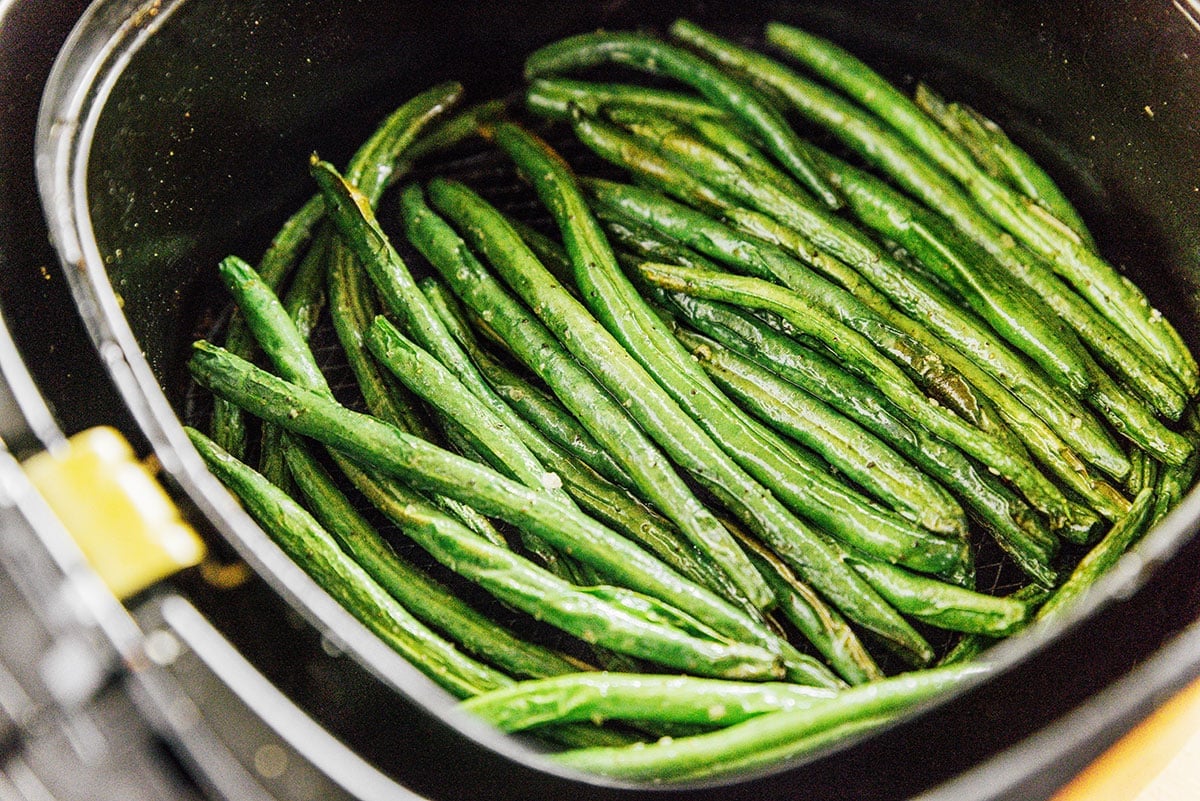 Crispy browned green beans in the basket of an air fryer.