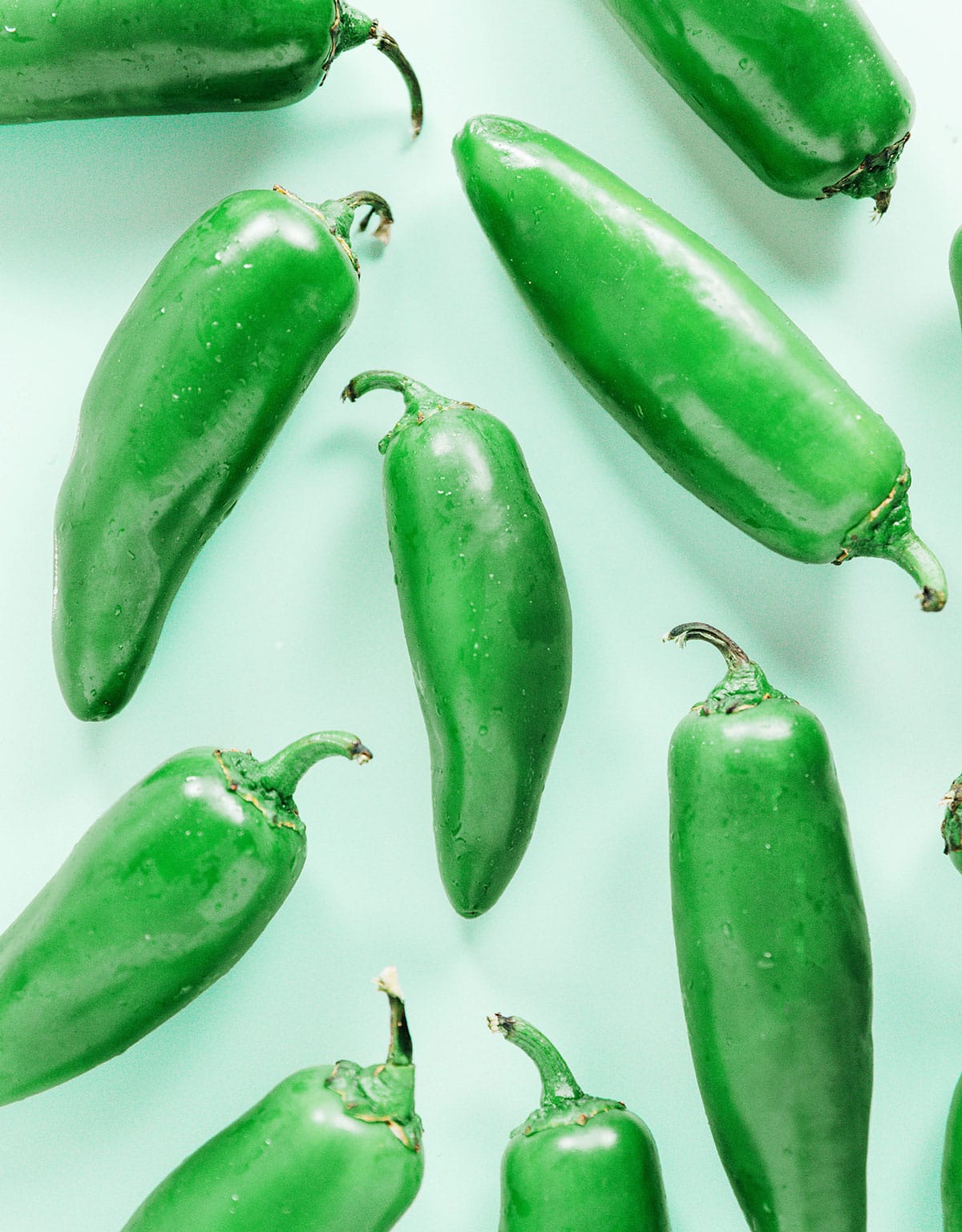 Fresh jalapeño peppers on a turquoise surface.