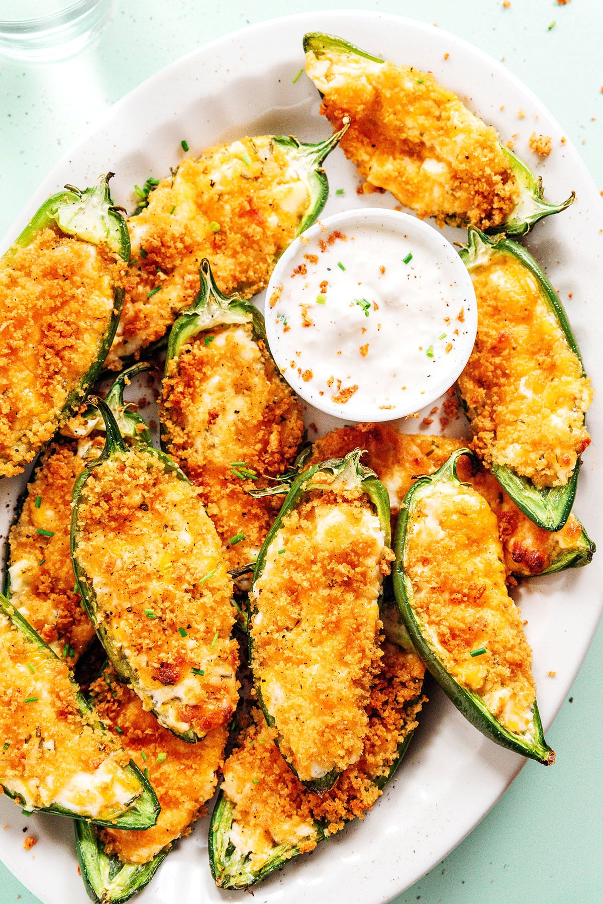 Vegetarian stuffed jalapeno poppers on a white serving platter with a bowl of dip.