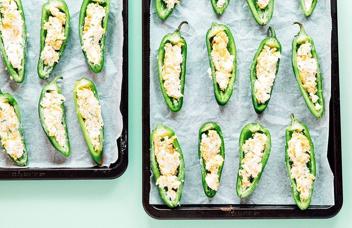Cheese stuffed jalapeno halves on a parchment lined baking sheet.