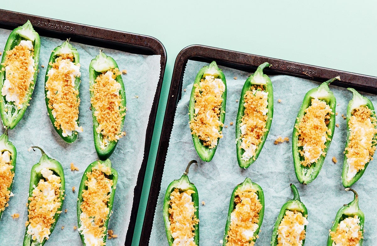 Jalapeno halves filled with cheese and topped with breadcrumbs on a parchment lined baking sheet.