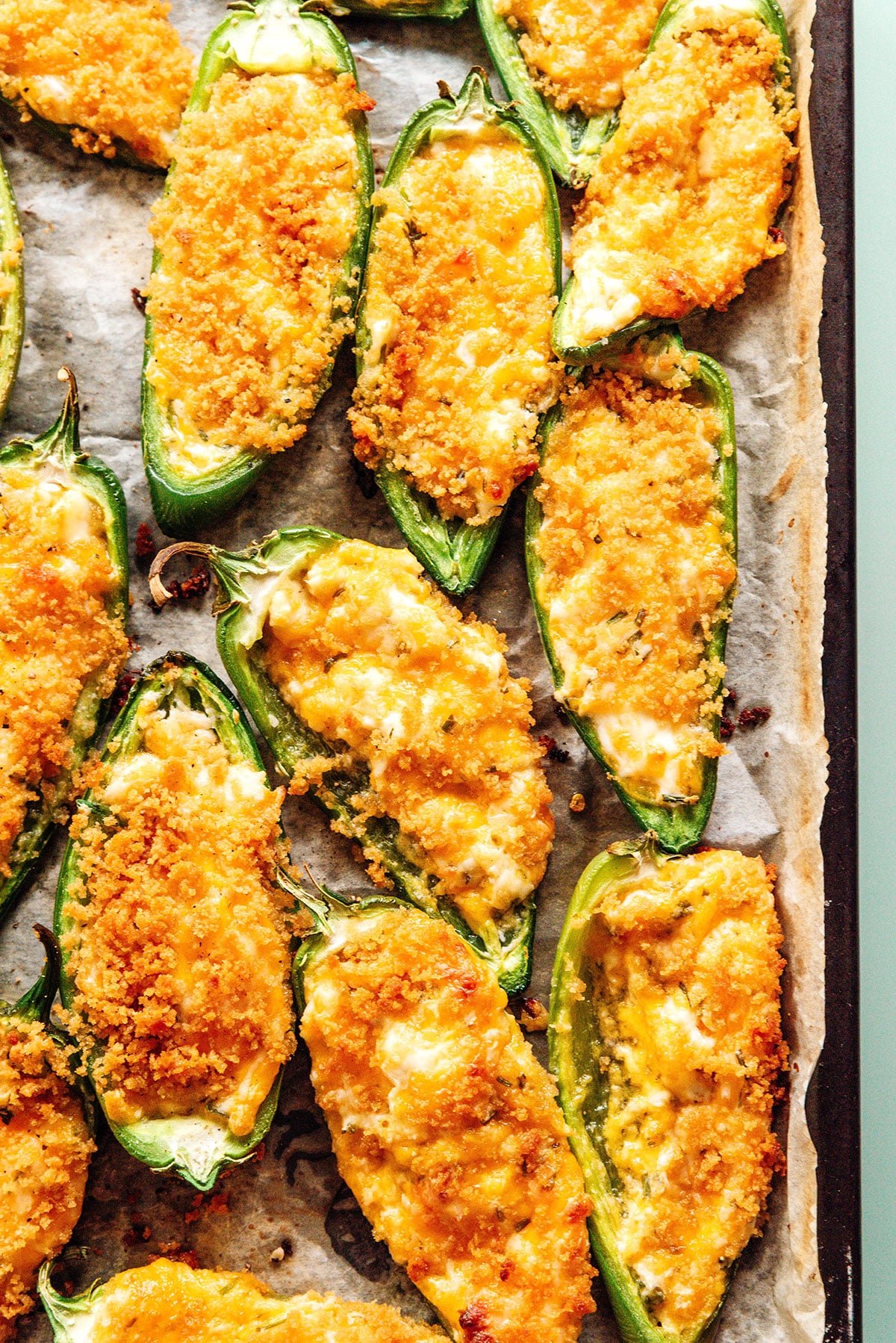 Baked vegetarian jalapeno poppers on a parchment lined baking sheet.
