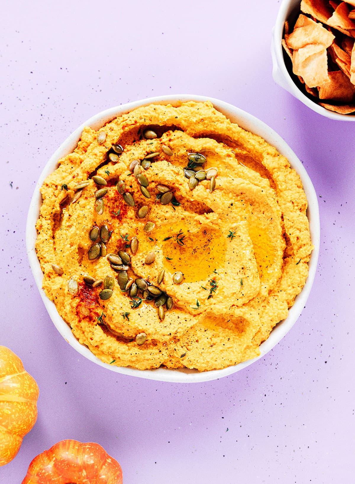 A large bowl of pumpkin hummus topped with pipits.