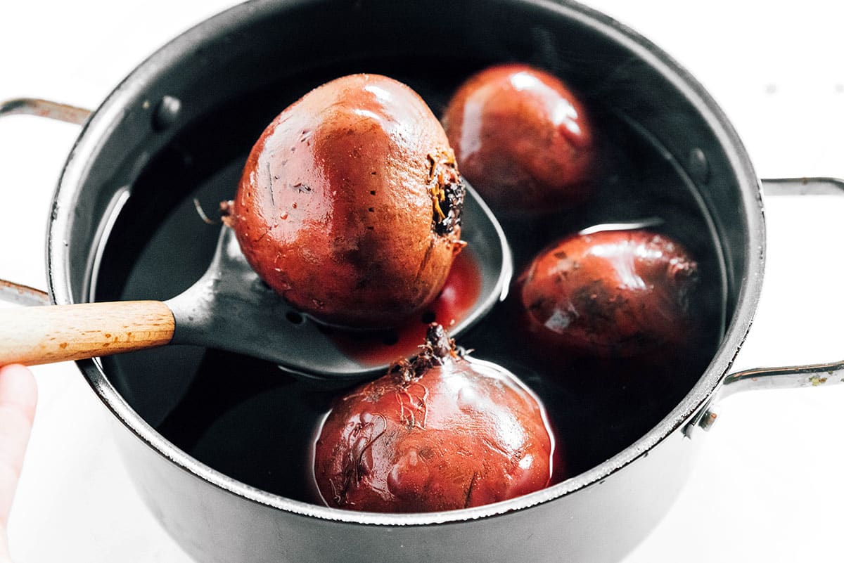 A slotted spoon lifting boiled beets from a pot of water.