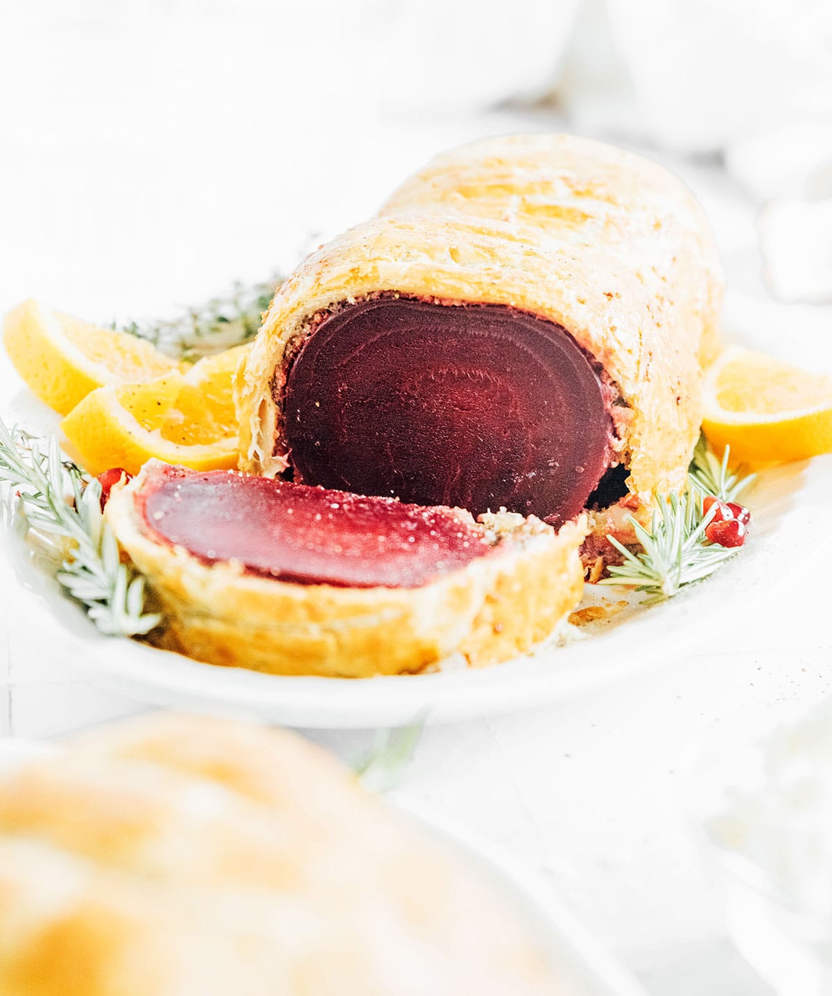 Beet Wellington on a serving platter with sprigs of rosemary and sliced oranges.