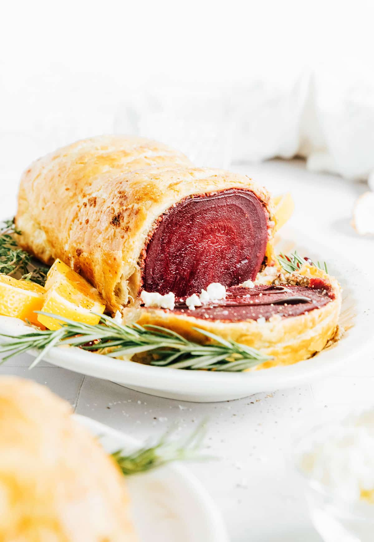 Vegan beet wellington on a serving platter next to rosemary and oranges.