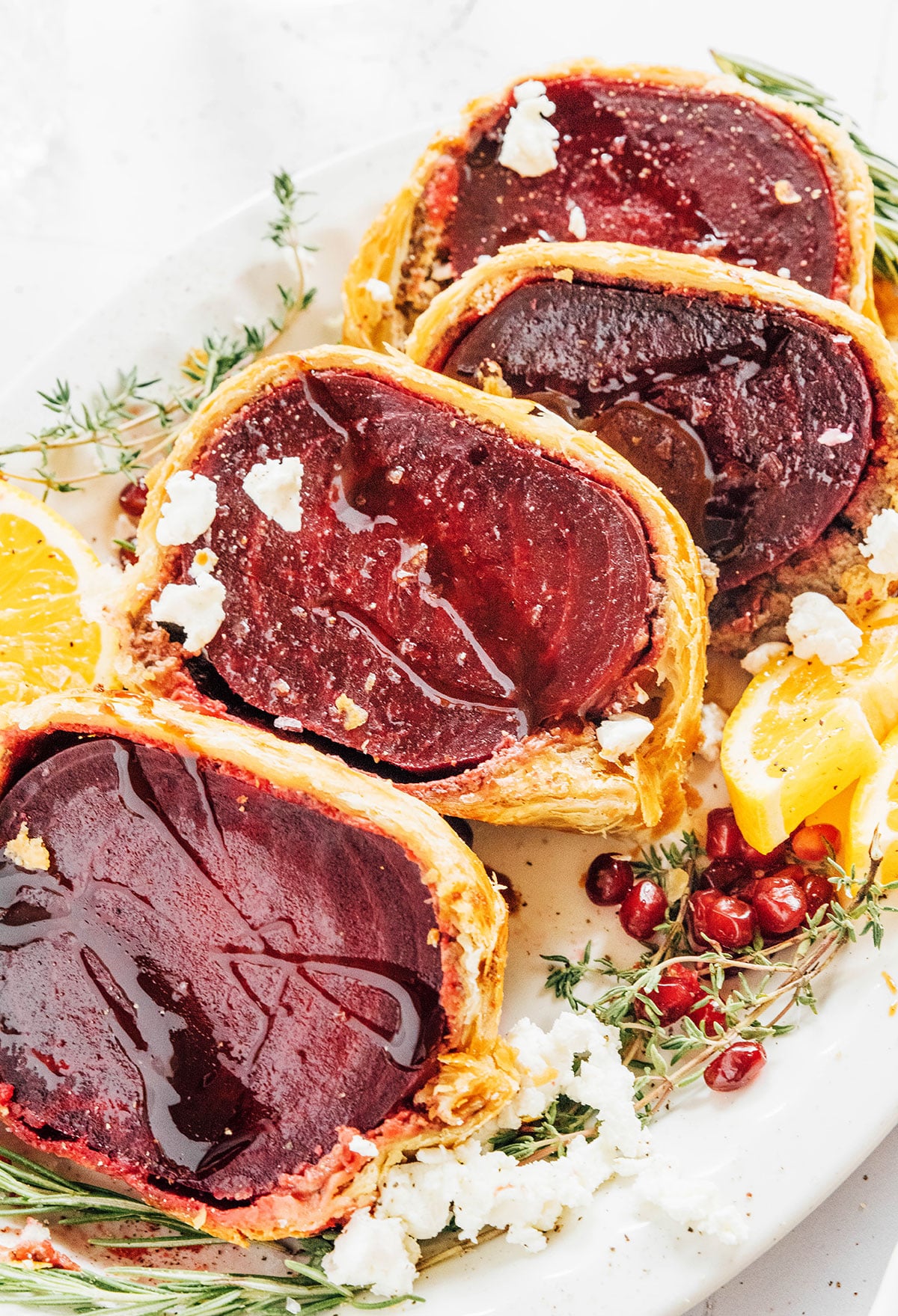 Slices of beet Wellington on a serving platter with fresh herbs and orange slices.