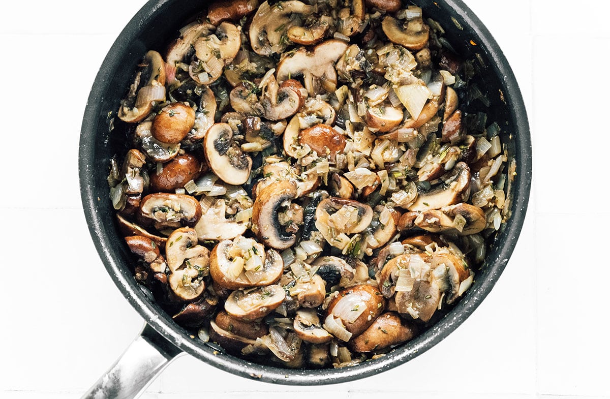 Mushrooms added to a saucepan of garlic and onions.