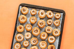 A baking tray lined with parchment paper holds rows of raw, hollowed-out mushrooms, all positioned with their caps facing down—perfectly prepped for making delicious vegetarian stuffed mushrooms.