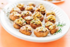 A white platter with vegetarian stuffed mushrooms, topped with a breadcrumb and herb mixture, arranged neatly for serving.