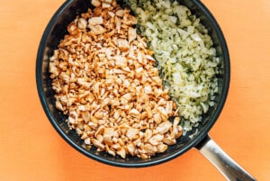 A frying pan contains chopped mushrooms on one side and diced onions on the other, set on an orange surface—perfect ingredients for preparing delicious vegetarian stuffed mushrooms.