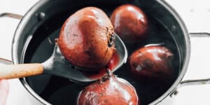 Four whole beets are being boiled in a pot of water; one beet, perfect for a savory beet Wellington, is being lifted out with a slotted spoon.