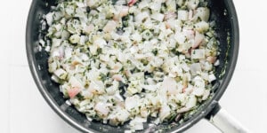 Chopped onions and herbs sautéing in a black frying pan—perfect for starting your beet wellington.