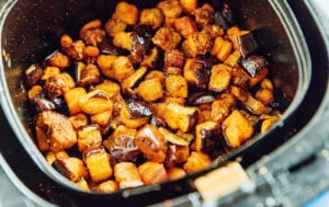 Cubed pieces of air fryer eggplant are seasoned and cooked, featuring dark purple skin with crispy, golden-brown edges.