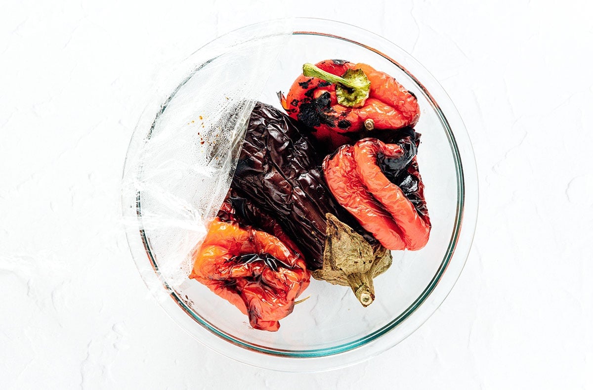 Roasted red peppers and an eggplant in a glass mixing bowl.