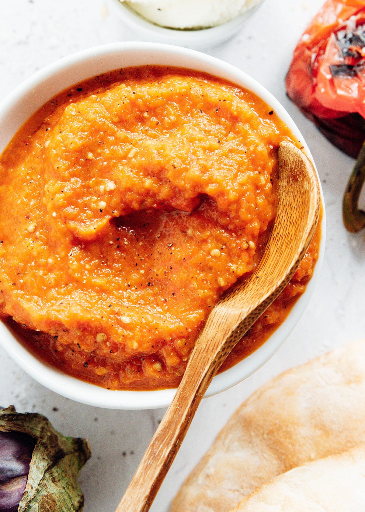 A wooden spoon in a small white bowl of ajvar sauce.