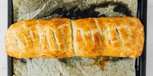 A baked golden-brown beet wellington loaf with slits on top, resting on parchment paper on a baking tray.