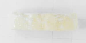 A block of butter wrapped in plastic sits on a white tiled surface, ready to be used in recipes like a classic beet wellington.