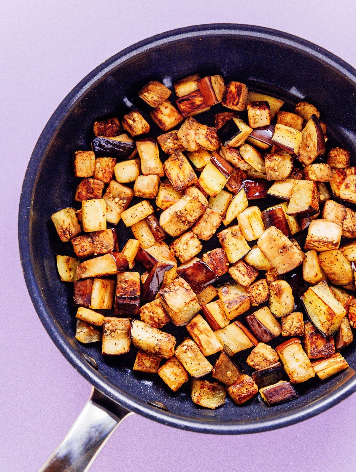 Diced eggplant that is golden brown in a saute pan.
