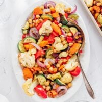 Rainbow colored Mediterranean vegetables on a white serving platter with a serving spoon.