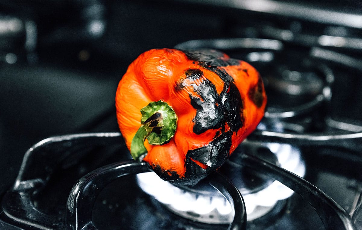 A red pepper being roasted on a gas stove top.