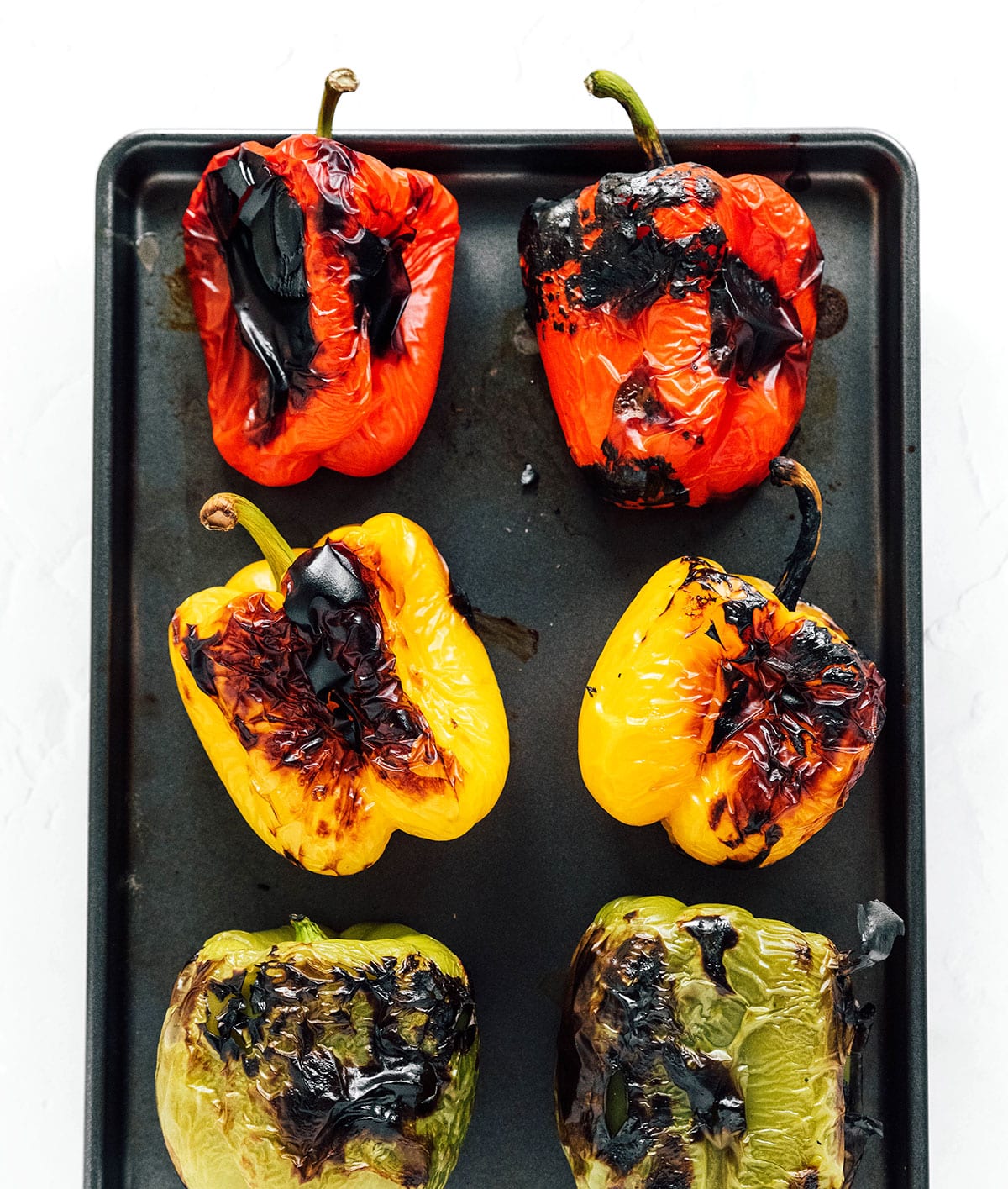 Red, green, and yellow peppers charred and laid out on a baking tray.