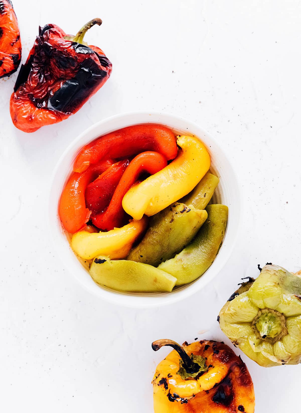 Roasted peppers in oil in a white bowl with roasted peppers next to it.