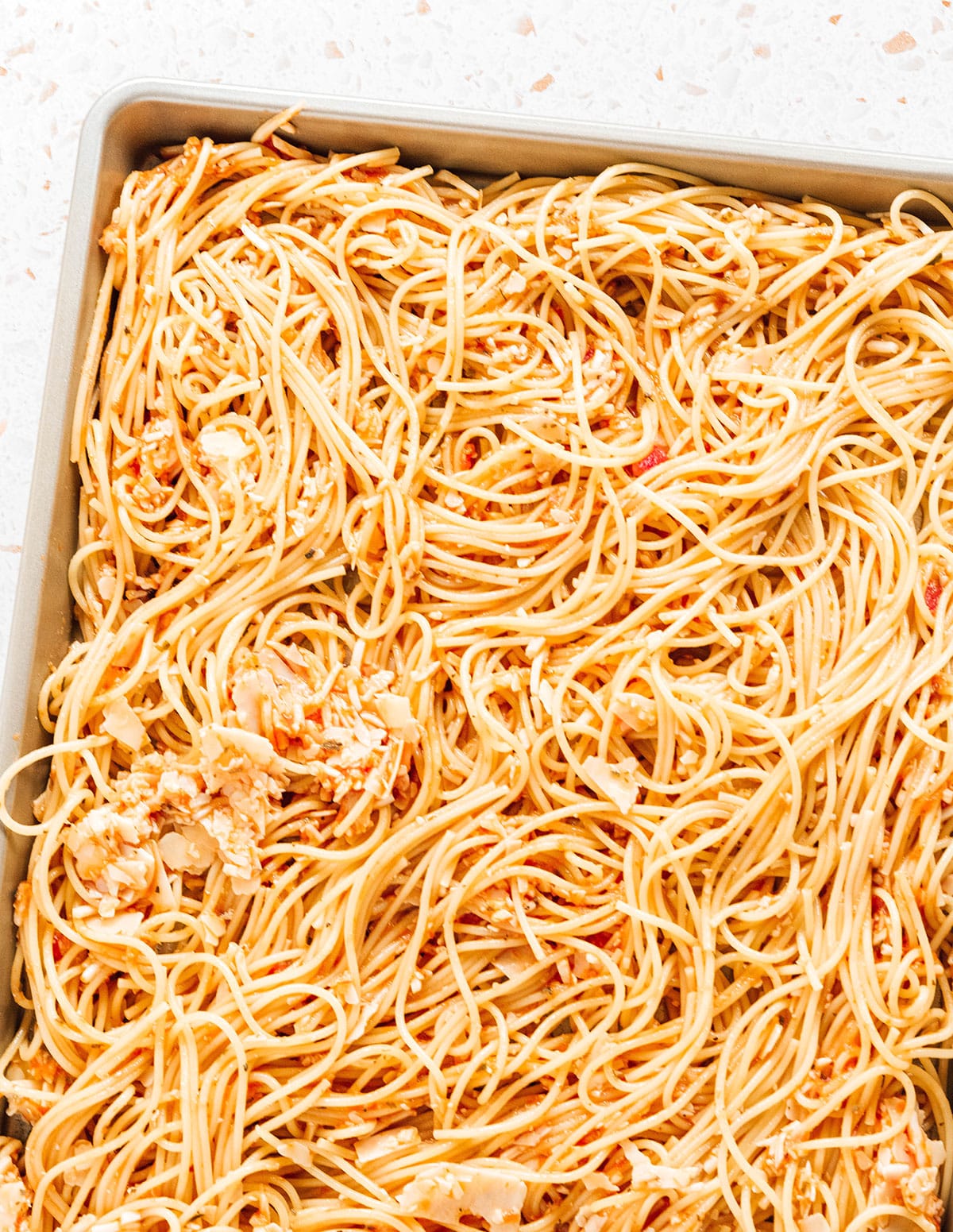 Sauce and cheese coated spaghetti spread in a baking dish.