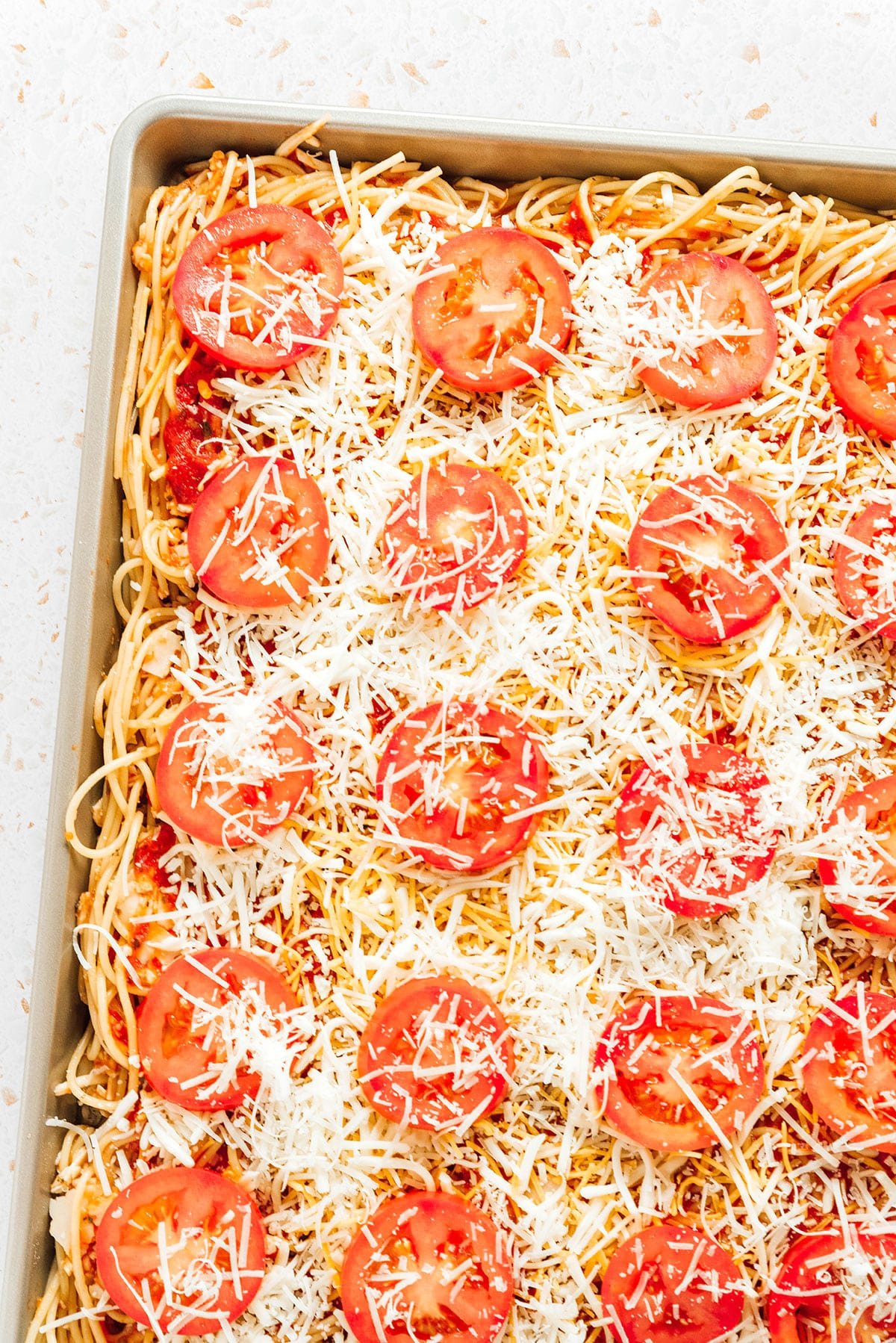 Sliced tomatoes and shredded cheese arranged over a pan of saucy spaghetti.