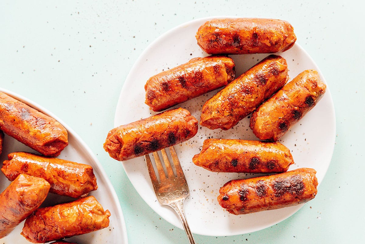 Plant based sausage links with a fork on a white plate.›