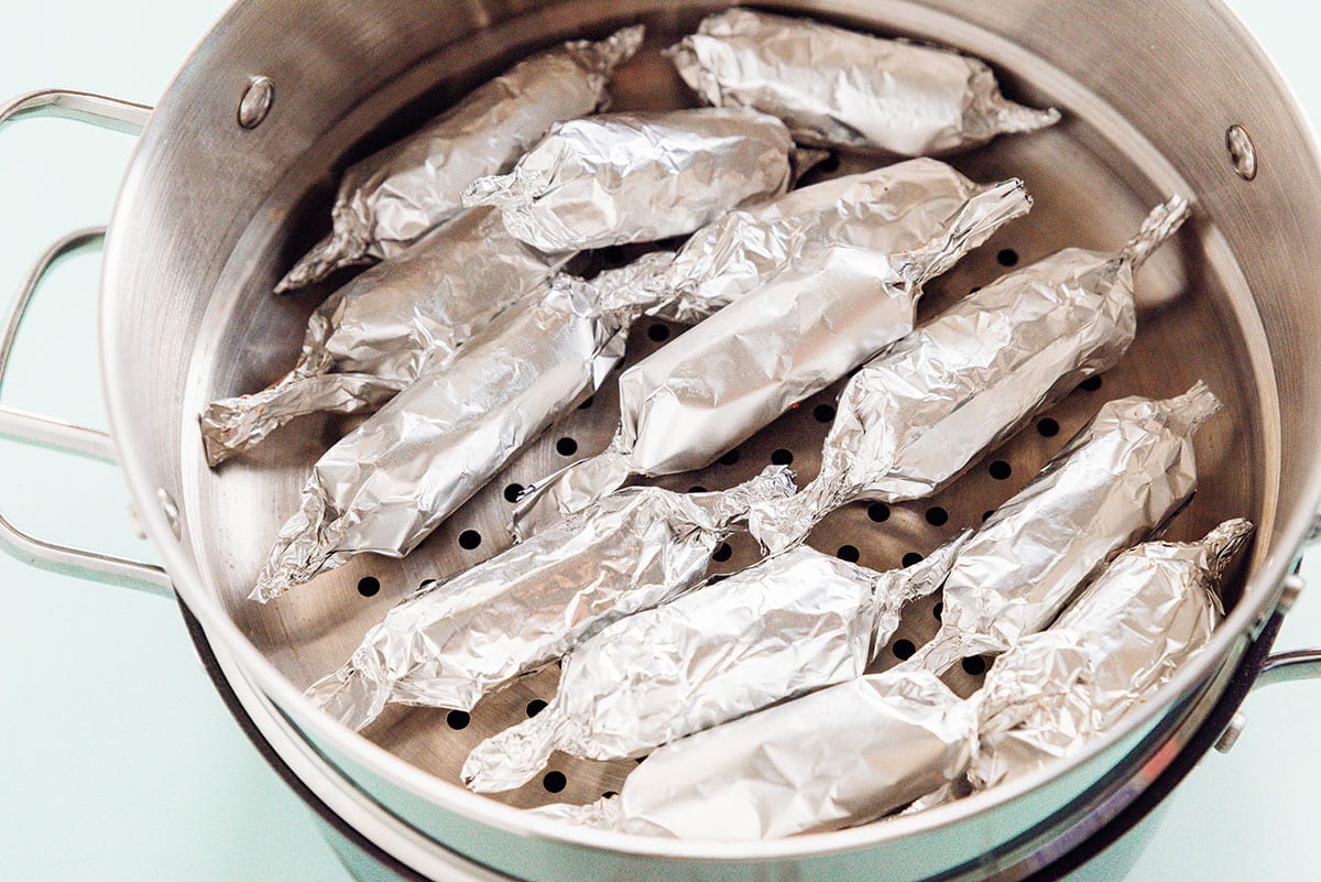 Foil-wrapped vegan sausages in a metal steamer basket.