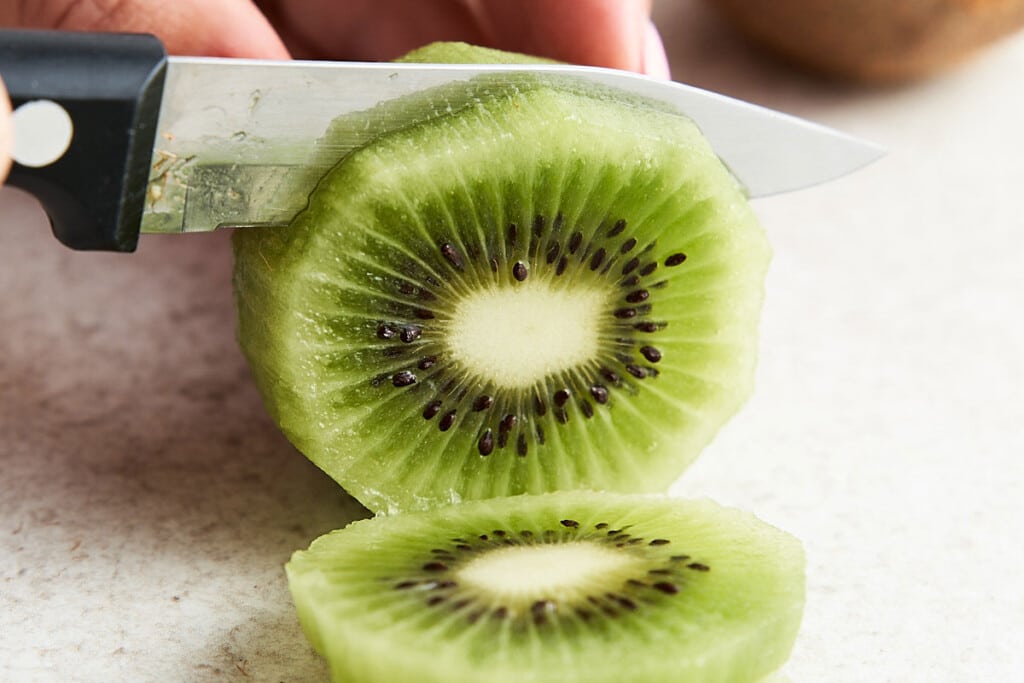Once you've peeled the kiwi, lay it on its side. Slice it crosswise into circles as thickly or as thinly as you'd prefer (around 1/8 or 1/4-inch).