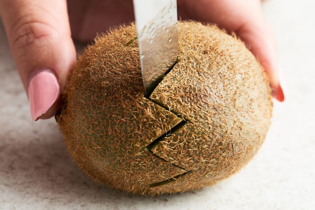Starting with the kiwi peel intact, lay it on its side with the stem end furthest away from you. Insert your paring knife all the way at a 45-degree angle.