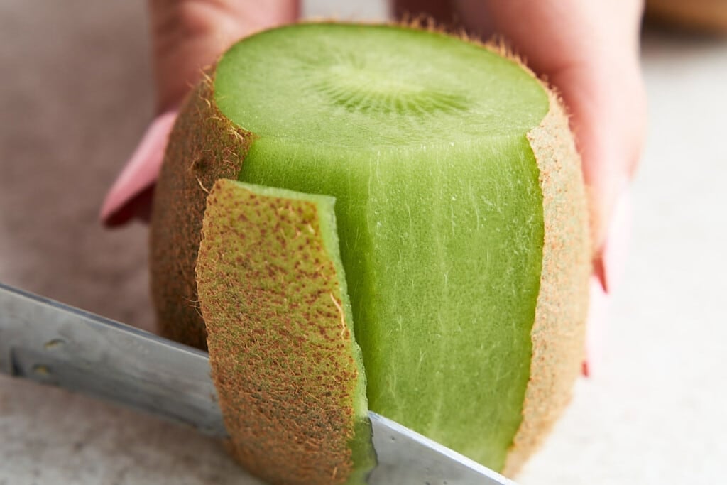 Peeling Option 1: Stand the kiwi on a flat side, then make vertical cuts where the skin meets the flesh. Follow the shape of the kiwi all the way down to prevent wasting any flesh.