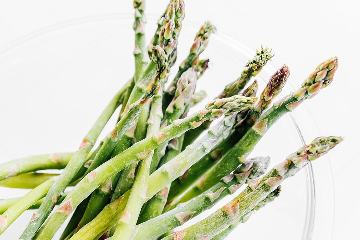 Frozen asparagus spears in a glass mixing bowl.