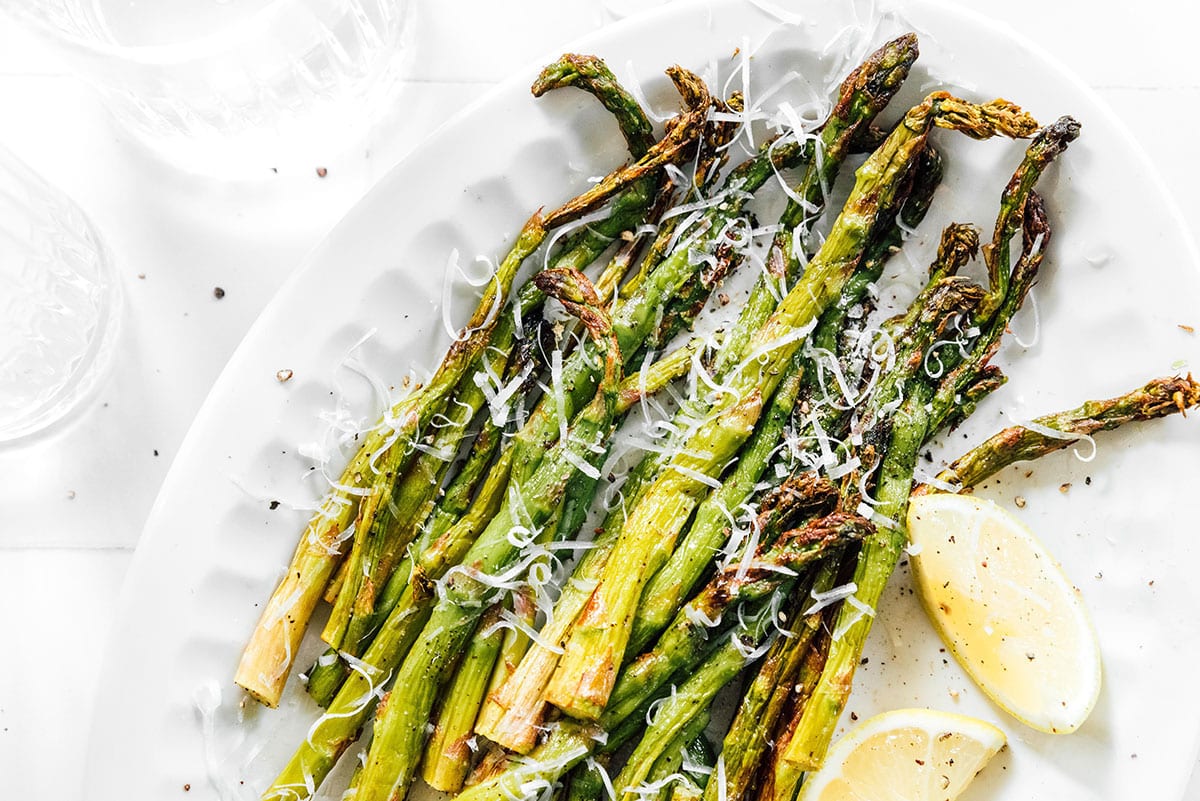 Air fried asparagus on a platter topped with Parmesan and lemon.
