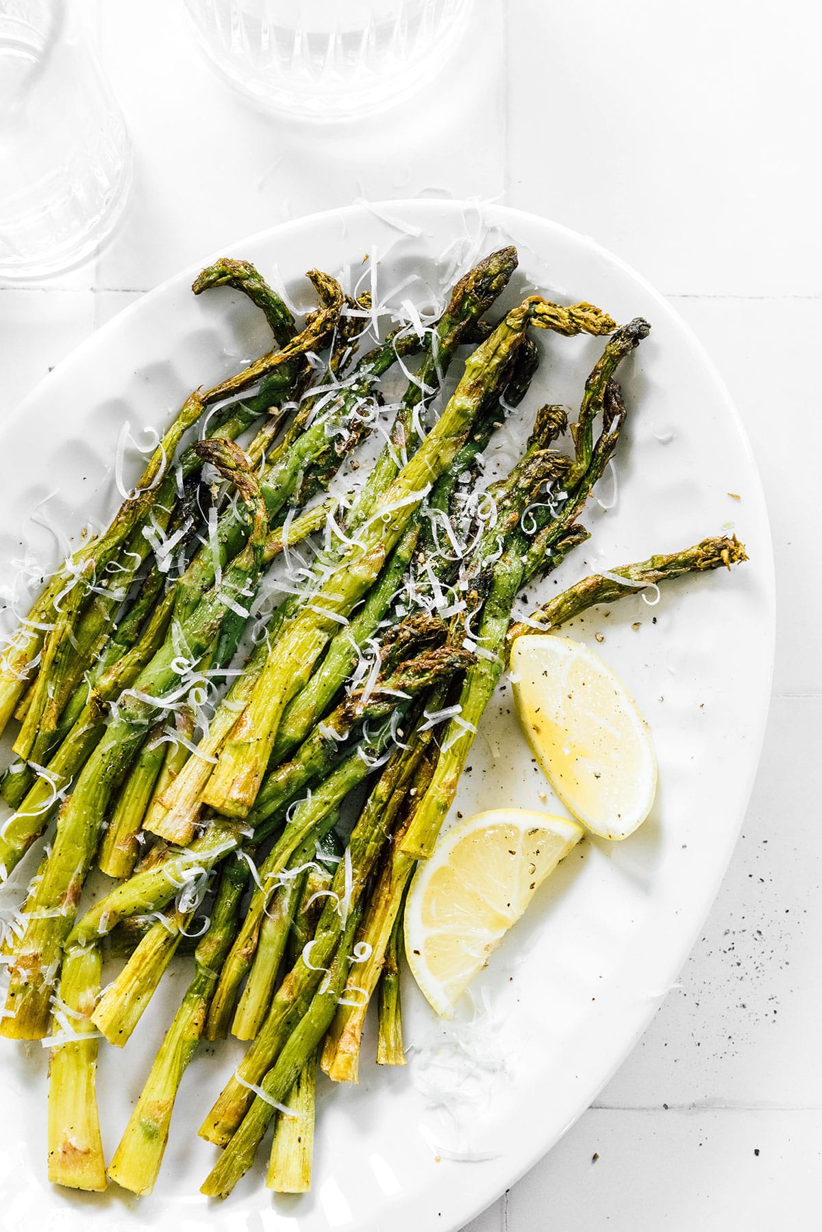 Air fried asparagus on a platter topped with Parmesan and lemon.