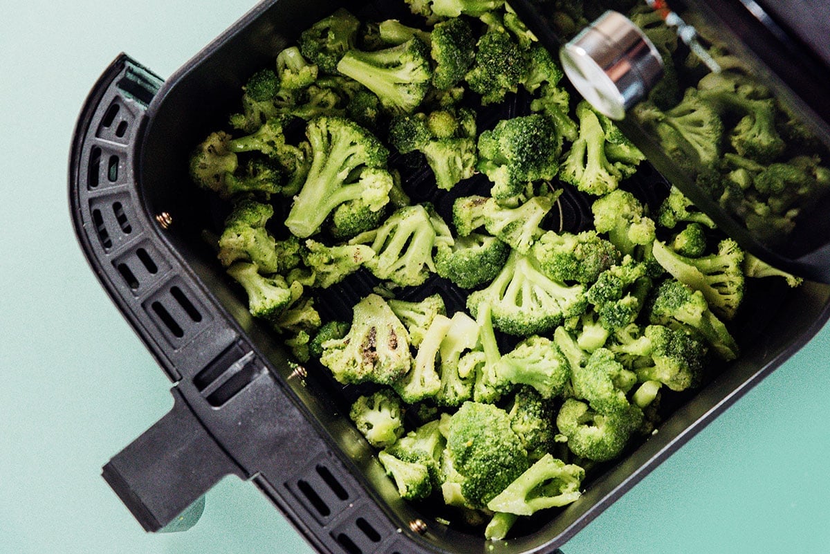Frozen broccoli florets in the basket of an air fryer.