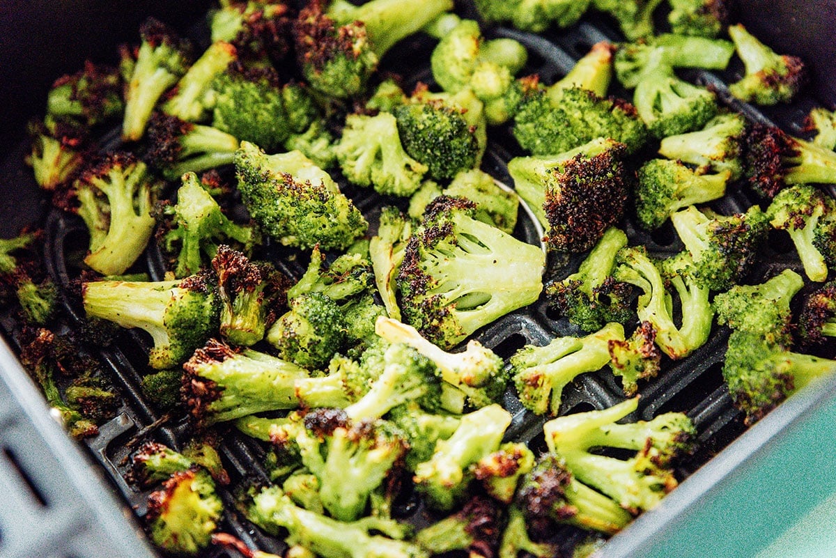 Frozen broccoli florets that are brown and crispy in the basket of an air fryer.